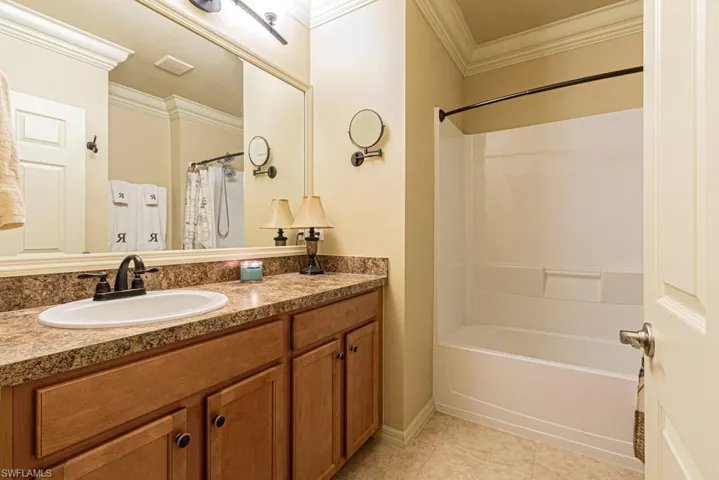 Bathroom featuring vanity, shower / bath combination with curtain, tile patterned floors, and crown molding