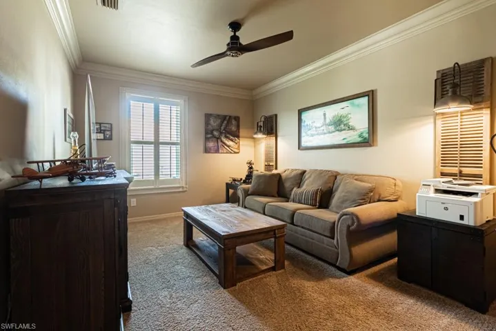 Carpeted living room featuring ceiling fan and crown molding