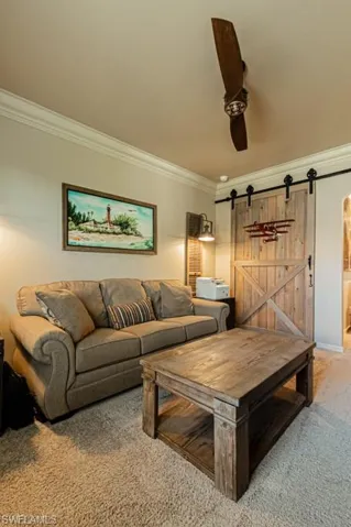 Living room with a barn door, carpet floors, and ornamental molding