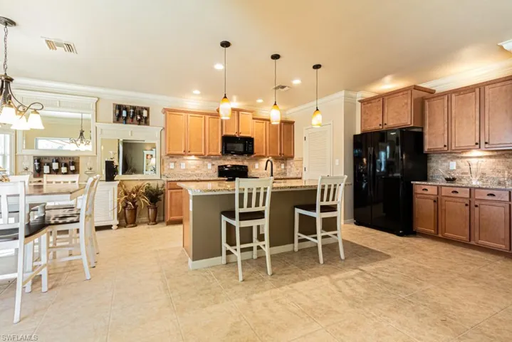Kitchen with black appliances, a chandelier, a breakfast bar area, an island with sink, and decorative light fixtures