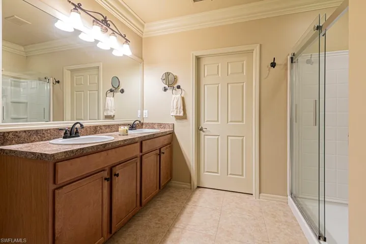 Bathroom with vanity, a shower with shower door, tile patterned flooring, and ornamental molding