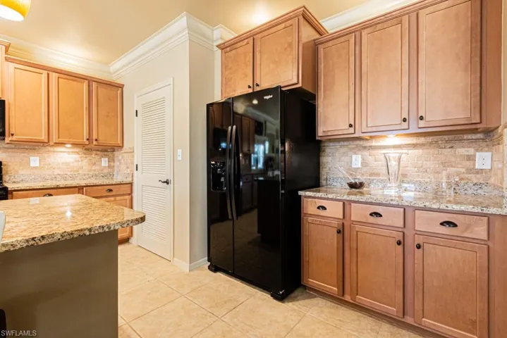 Kitchen featuring black fridge, decorative backsplash, light stone counters, and light tile patterned flooring