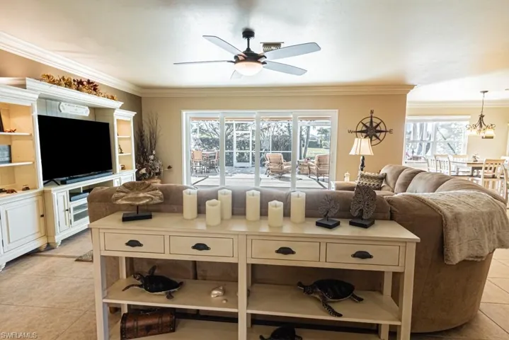 Tiled living room with ceiling fan with notable chandelier, plenty of natural light, and crown molding