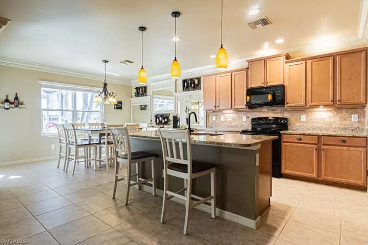 Kitchen featuring black appliances, a center island with sink, light stone countertops, hanging light fixtures, and sink