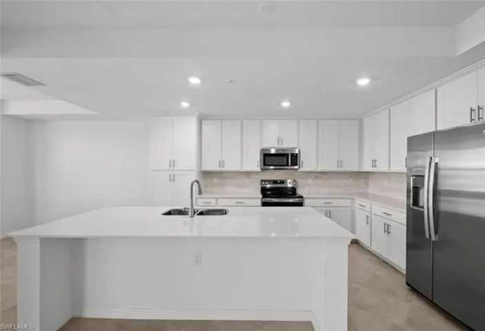 Kitchen featuring a sink, backsplash, light countertops, appliances with stainless steel finishes, and a kitchen island with sink