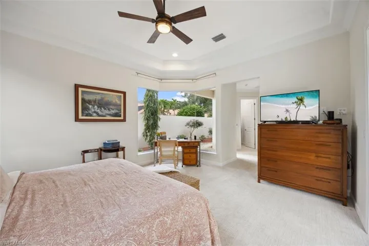 Carpeted bedroom with crown molding, ceiling fan, and a tray ceiling