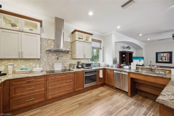Kitchen with stainless steel appliances, sink, light stone counters, ornamental molding, and wall chimney range hood