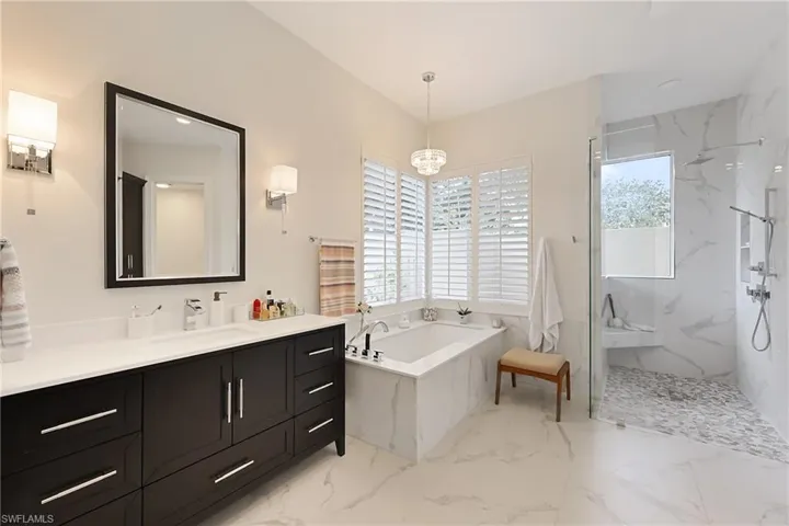 Primary Bathroom with dual vanities, an inviting chandelier, walk in shower with separate bathtub views to zen garden