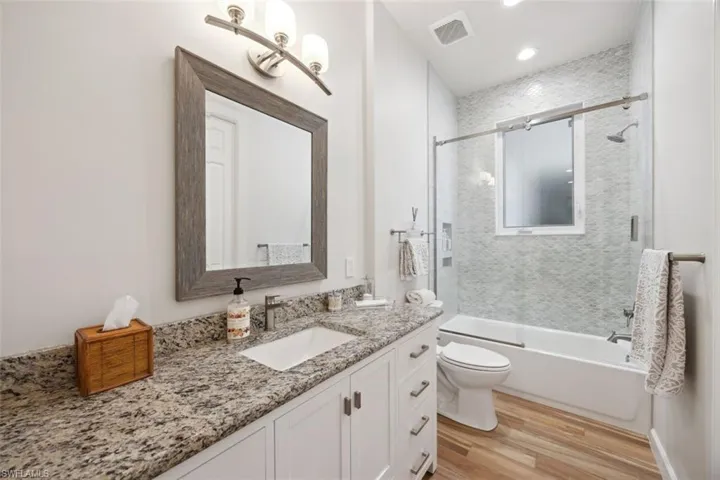 Full bathroom with toilet, vanity, wood-type flooring, and combined bath / shower with glass door