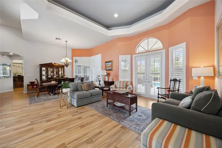 Living room with light hardwood / wood-style tile floors, french doors, a raised ceiling, and a notable chandelier