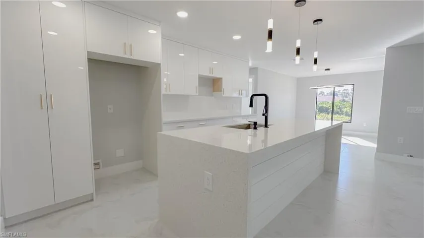 Kitchen with sink, light stone counters, light tile patterned floors, pendant lighting, and white cabinets