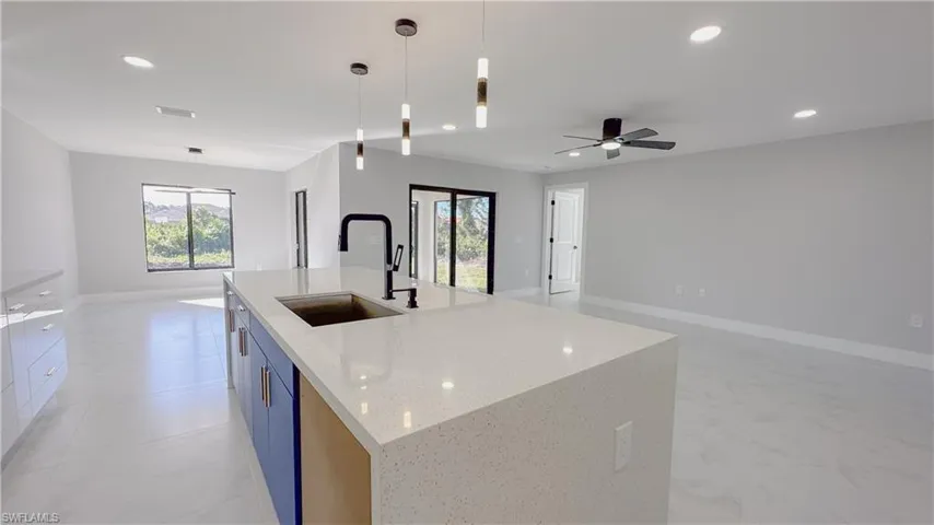 Kitchen featuring sink, light stone counters, an island with sink, light tile patterned floors, and ceiling fan