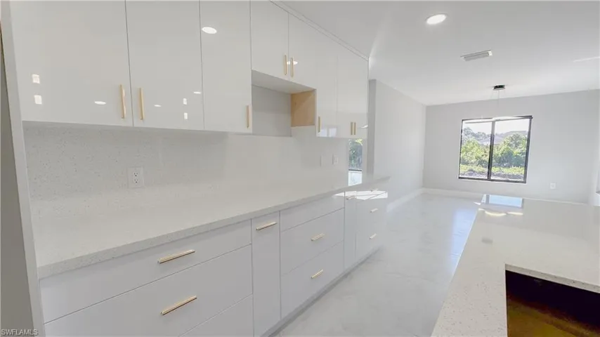 Kitchen featuring light tile patterned floors, backsplash, light stone counters, and white cabinetry