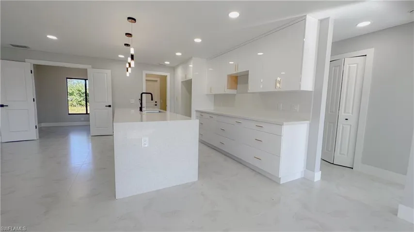 Kitchen with decorative light fixtures, white cabinetry, tasteful backsplash, sink, and light tile patterned floors