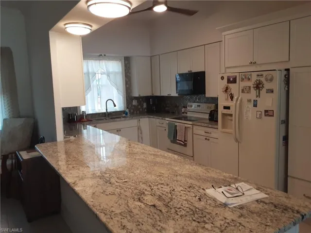 Kitchen with light stone counters, white appliances, white cabinets, and a peninsula
