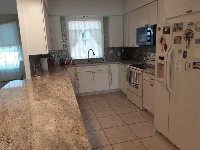Kitchen with white appliances, white cabinetry, light stone counters, light tile patterned floors, and backsplash