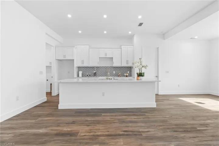 Kitchen with white cabinets, dark hardwood / wood-style flooring, and a center island with sink