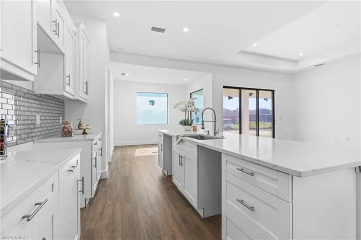 Kitchen featuring decorative backsplash, dark wood-type flooring, a spacious island, sink, and white cabinets