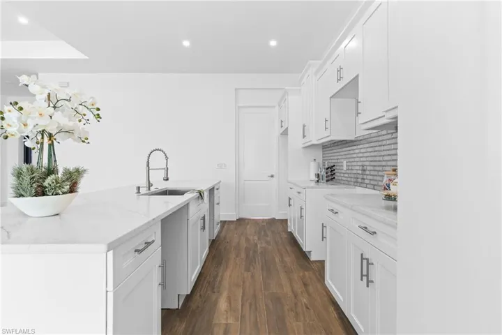Kitchen featuring light stone countertops, dark hardwood / wood-style flooring, white cabinetry, and sink