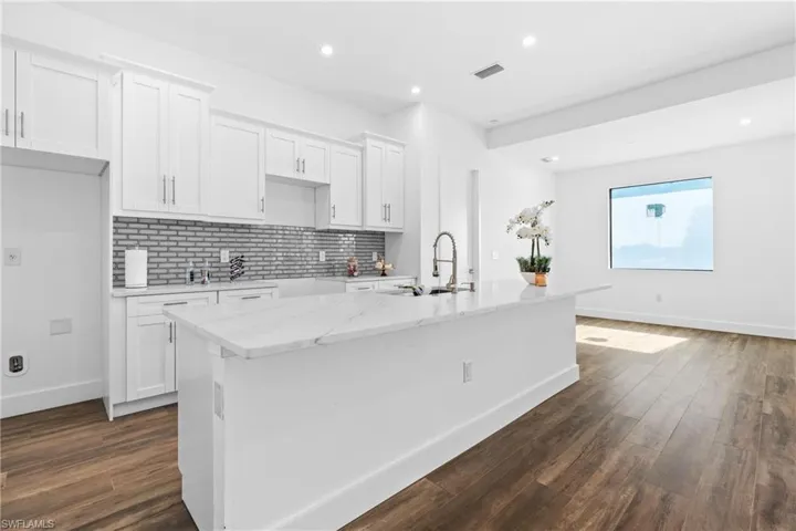 Kitchen featuring dark hardwood / wood-style flooring, white cabinetry, a kitchen island with sink, and sink
