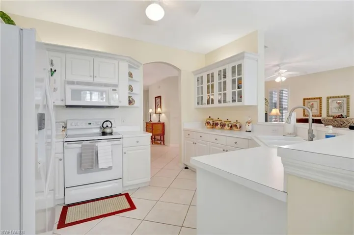 Kitchen with white appliances, light tile patterned floors, a sink, arched walkways, and a ceiling fan