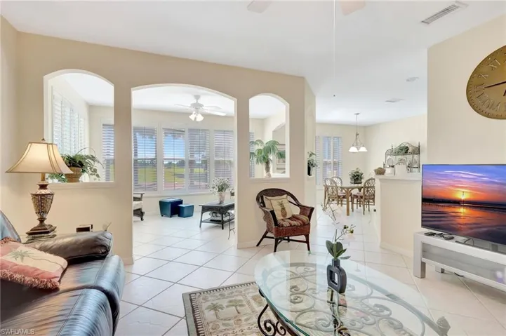 Living room with light tile patterned floors, arched walkways, visible vents, a wealth of natural light, and ceiling fan