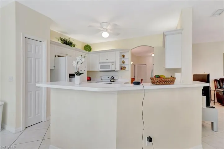 Kitchen featuring a peninsula, white appliances, arched walkways, open shelves, and light tile patterned floors
