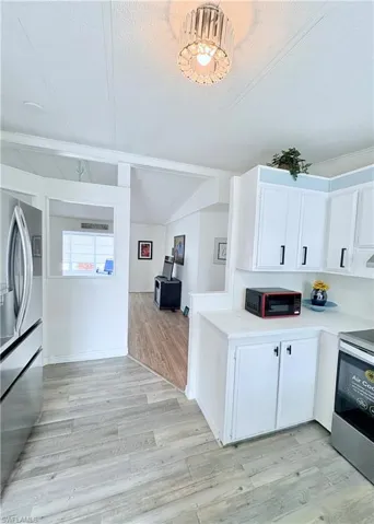Kitchen featuring white cabinets, stainless steel appliances, light wood-type flooring, open floor plan, and a textured ceiling