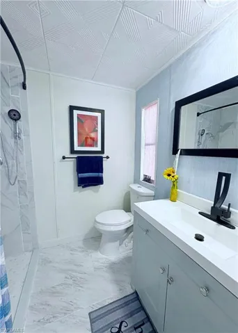 Bathroom with a marble finish shower, light marble finish flooring, and vanity
