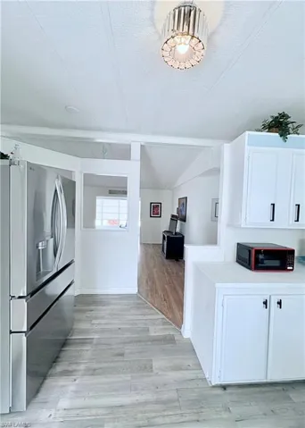 Kitchen featuring stainless steel fridge, white cabinets, light wood finished floors, a textured ceiling, and black microwave