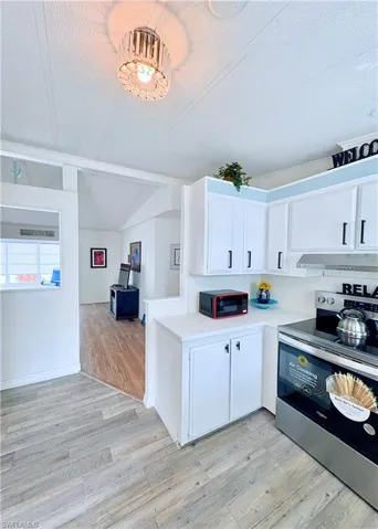 Kitchen featuring stainless steel electric stove, white cabinets, a textured ceiling, light wood-style flooring, and light countertops