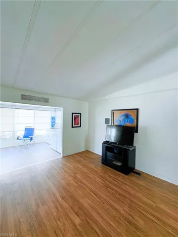 Unfurnished living room featuring wood finished floors and vaulted ceiling
