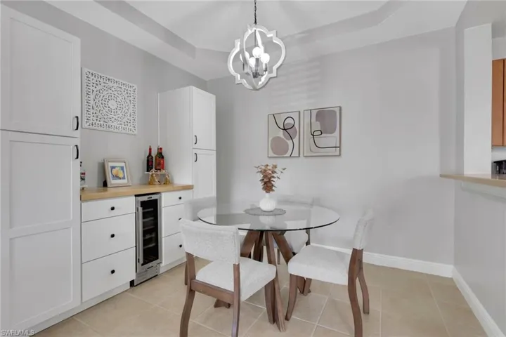 Dining space with beverage cooler, a tray ceiling, light tile patterned floors, and hanging lights