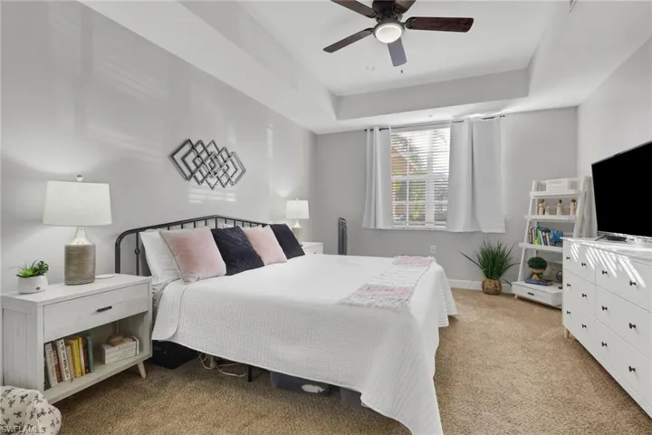 Bedroom featuring light carpet, a tray ceiling, and ceiling fan