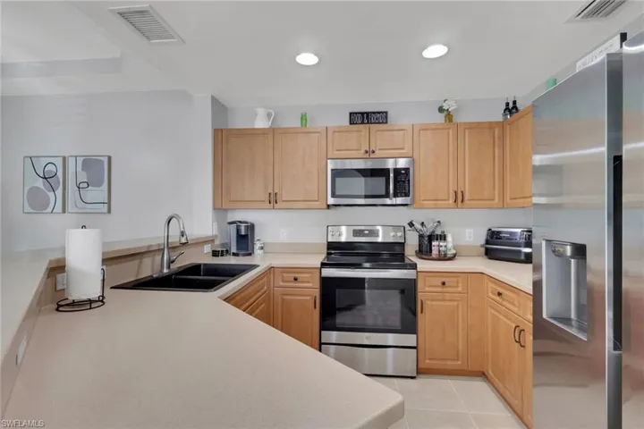 Kitchen with stainless steel appliances, light countertops, light tile patterned flooring, light wood finish cabinets, and a peninsula