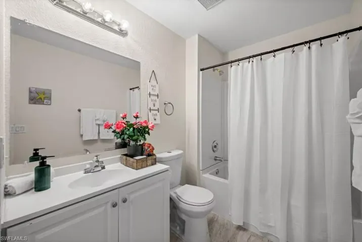 Bathroom featuring vanity, shower / bath combo with shower curtain, light wood finished floors, and a textured wall