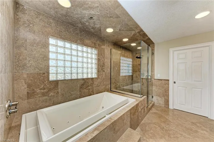 Bathroom featuring shower with separate bathtub, a textured ceiling, and tile walls