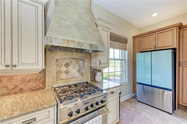 Kitchen featuring decorative backsplash, stainless steel appliances, light stone counters, and wall chimney range hood