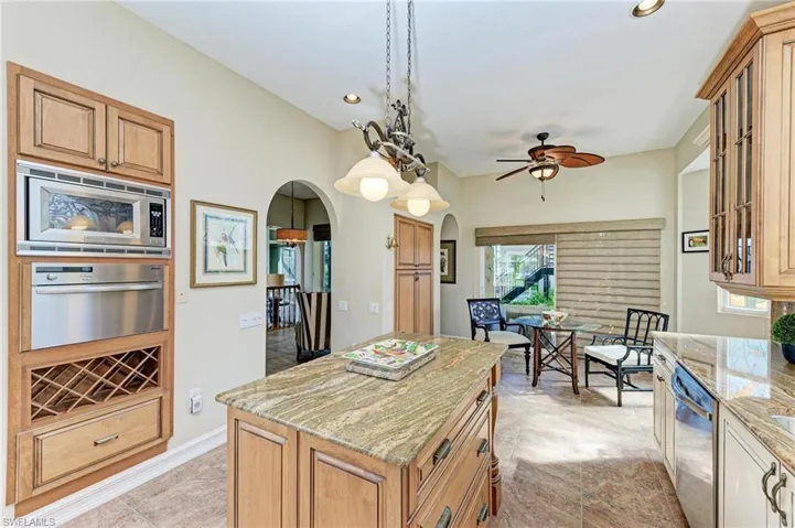 Kitchen with light stone countertops, a center island, ceiling fan, decorative light fixtures, and appliances with stainless steel finishes