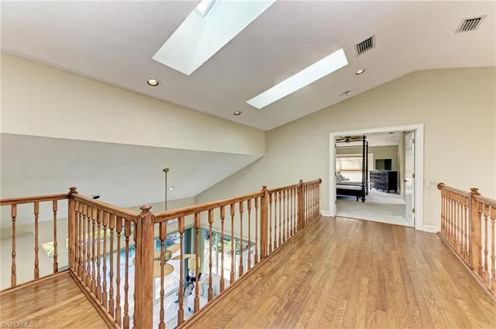 Corridor featuring vaulted ceiling with skylight and light wood-type flooring