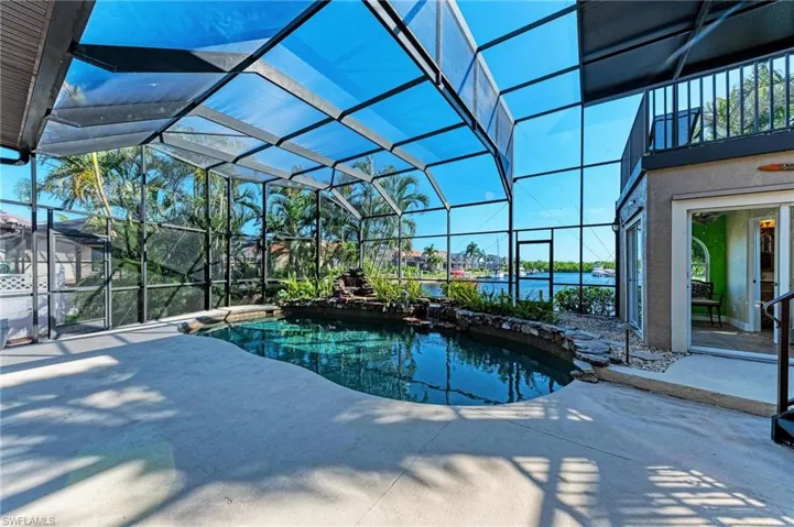 View of swimming pool featuring glass enclosure, a patio area, and a water view