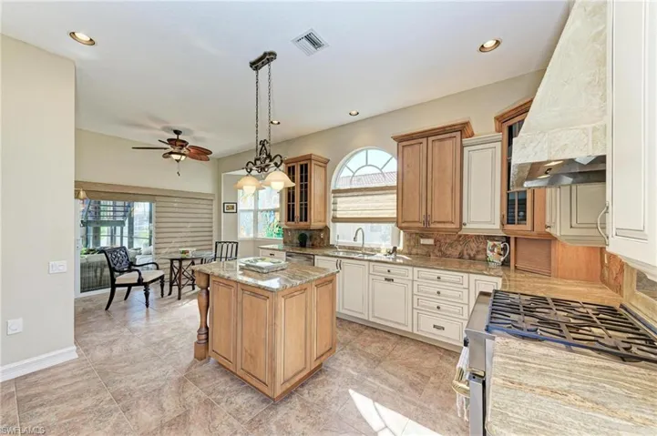 Kitchen featuring ceiling fan, sink, light stone counters, a kitchen island, and custom range hood