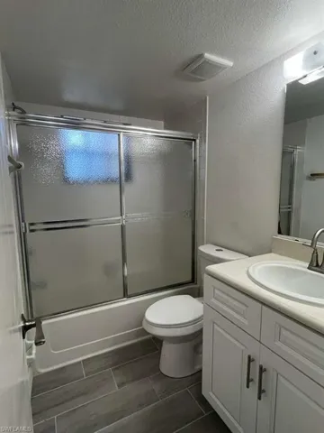 Bathroom with vanity, a textured ceiling, combined bath / shower with glass door, and a textured wall