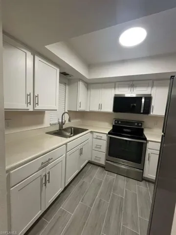 Kitchen featuring stainless steel electric range, white cabinets, light countertops, and freestanding refrigerator