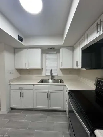 Kitchen featuring range with electric stovetop, white cabinets, light countertops, and stainless steel microwave