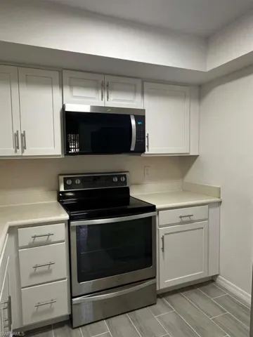 Kitchen with appliances with stainless steel finishes, white cabinetry, light countertops, and wood finish floors