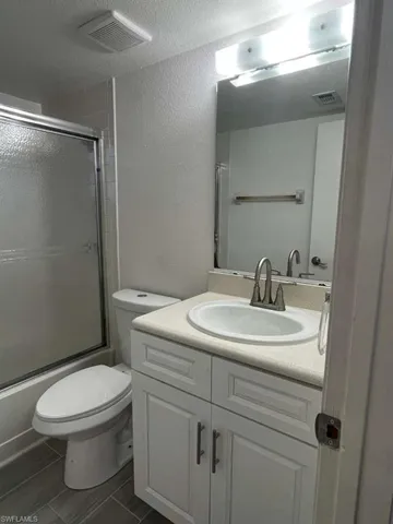 Full bath featuring vanity, combined bath / shower with glass door, a textured ceiling, and a textured wall