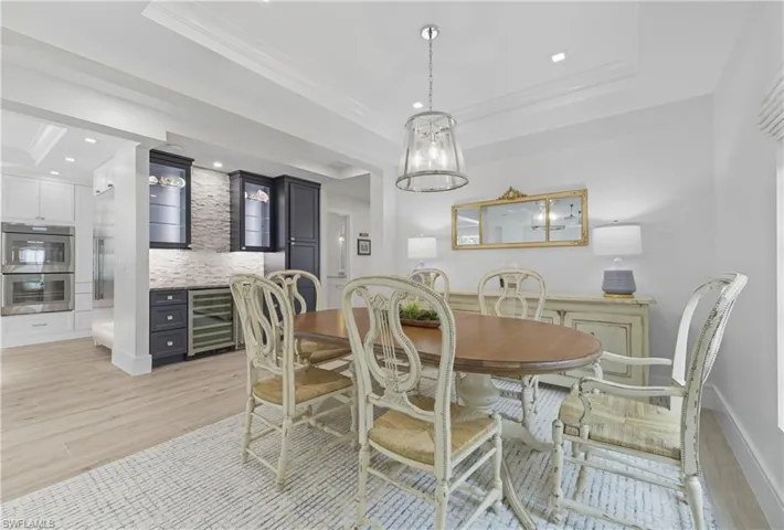 Dining space featuring a tray ceiling, beverage cooler, light wood-style floors, and ornamental molding