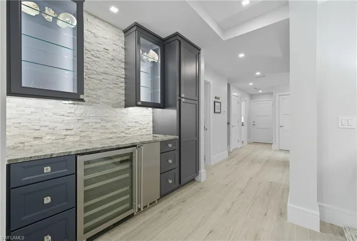 Bar area featuring beverage cooler, light stone counters, light wood finished floors, glass insert cabinets, and recessed lighting