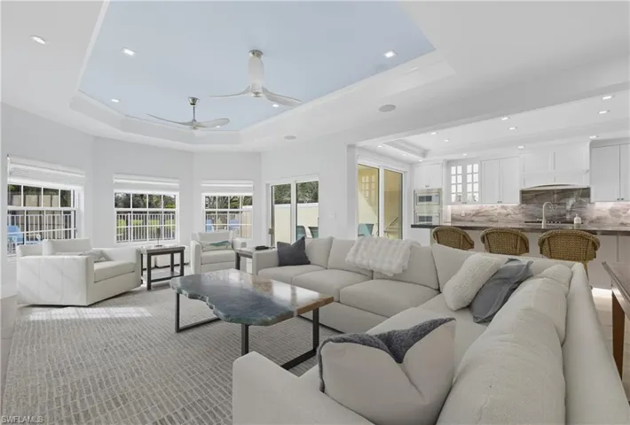 Living room with a tray ceiling, recessed lighting, and a ceiling fan